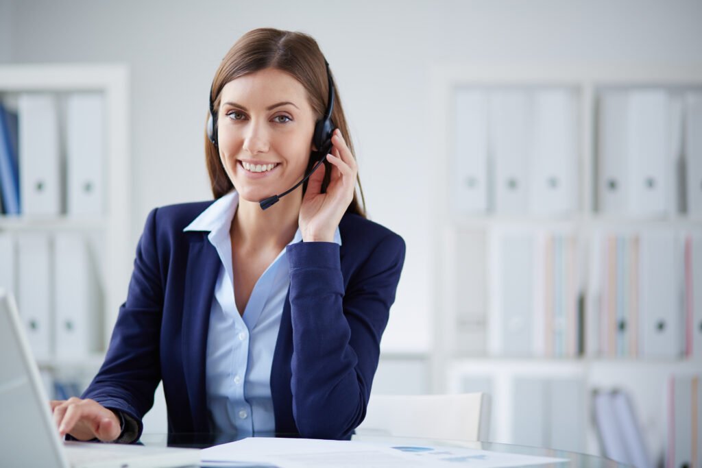 A Woman Wearing A Headset Sits At A Desk, Focused On Her Work With A Computer In Front Of Her.