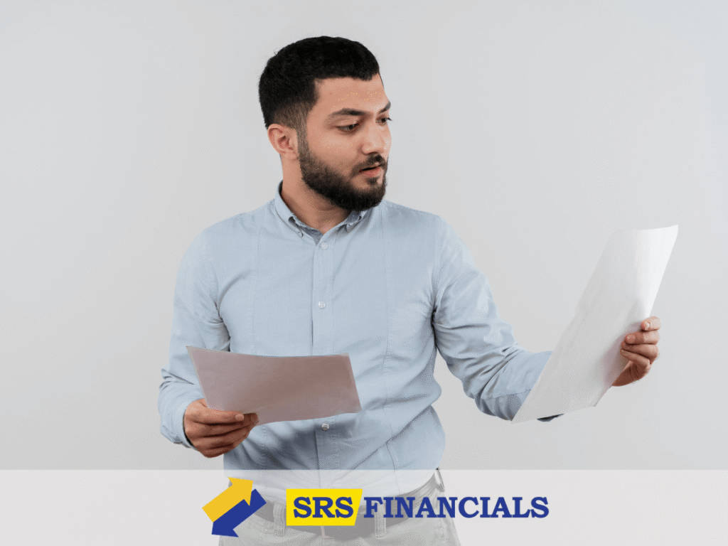 A Man Reading A Pay Stubs Titled &Quot;Srs Financials,&Quot; Focused On The Text In A Well-Lit Office Setting.