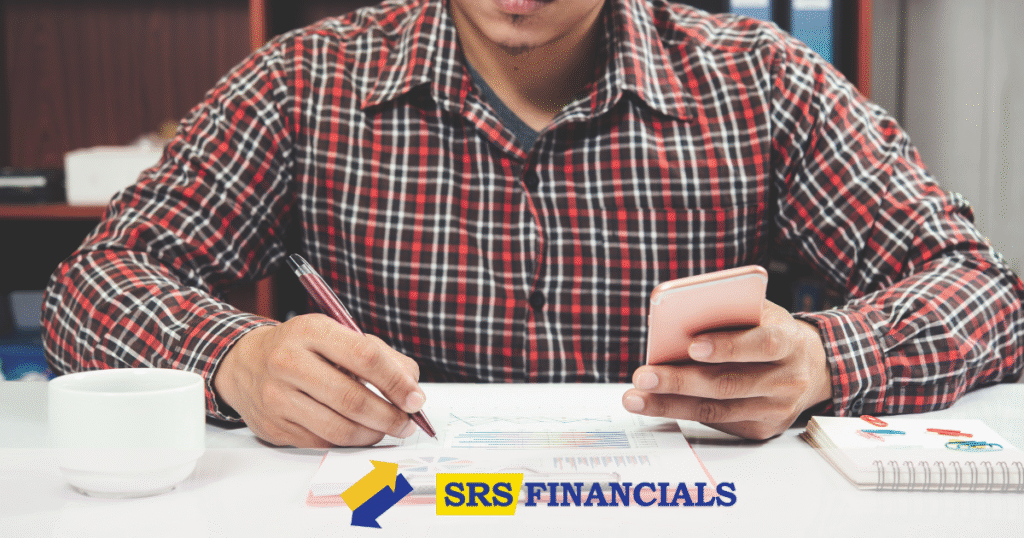 A man in a plaid shirt is focused on writing on his phone, possibly analyzing his annual salary before and after taxes.