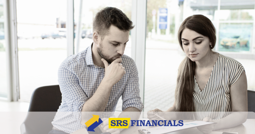 A man and woman seated at a table discussing SRS financials, with documents and a laptop in front of them.